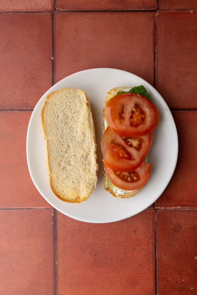 Stacking lettuce and tomato on top of bread with tartar sauce to make a salmon sandwich. 