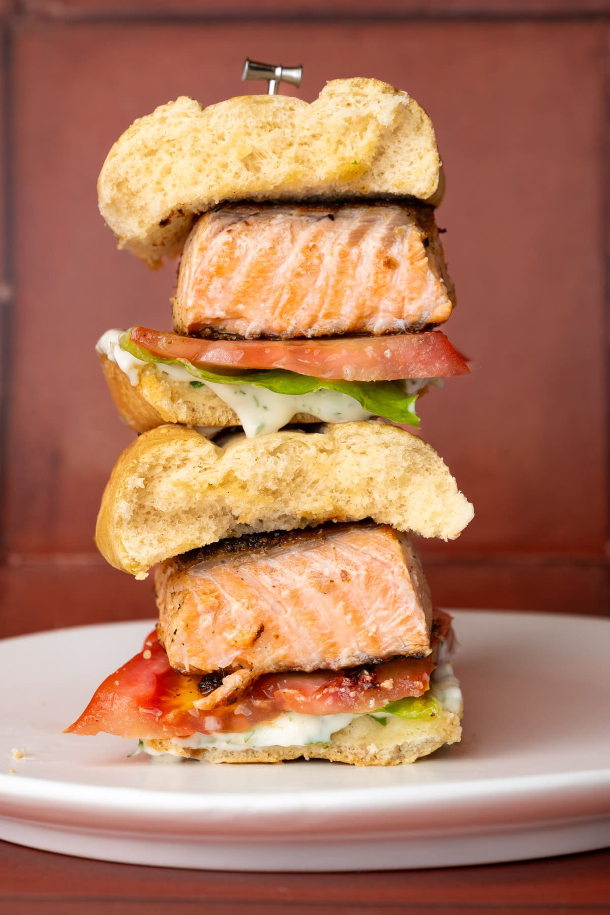 Salmon sandwich with tomato and lettuce sliced in half with halves stacked on top of one another. 