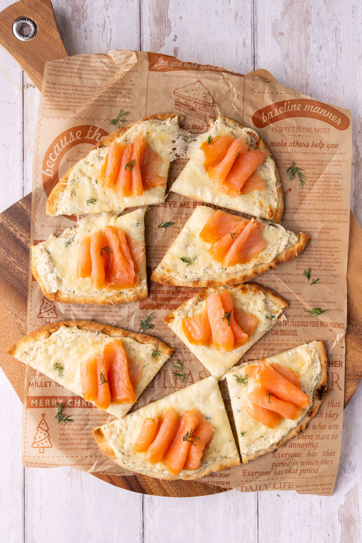 Overhead image of two sliced naan smoked salmon flatbreads on a cutting board with parchment paper. 