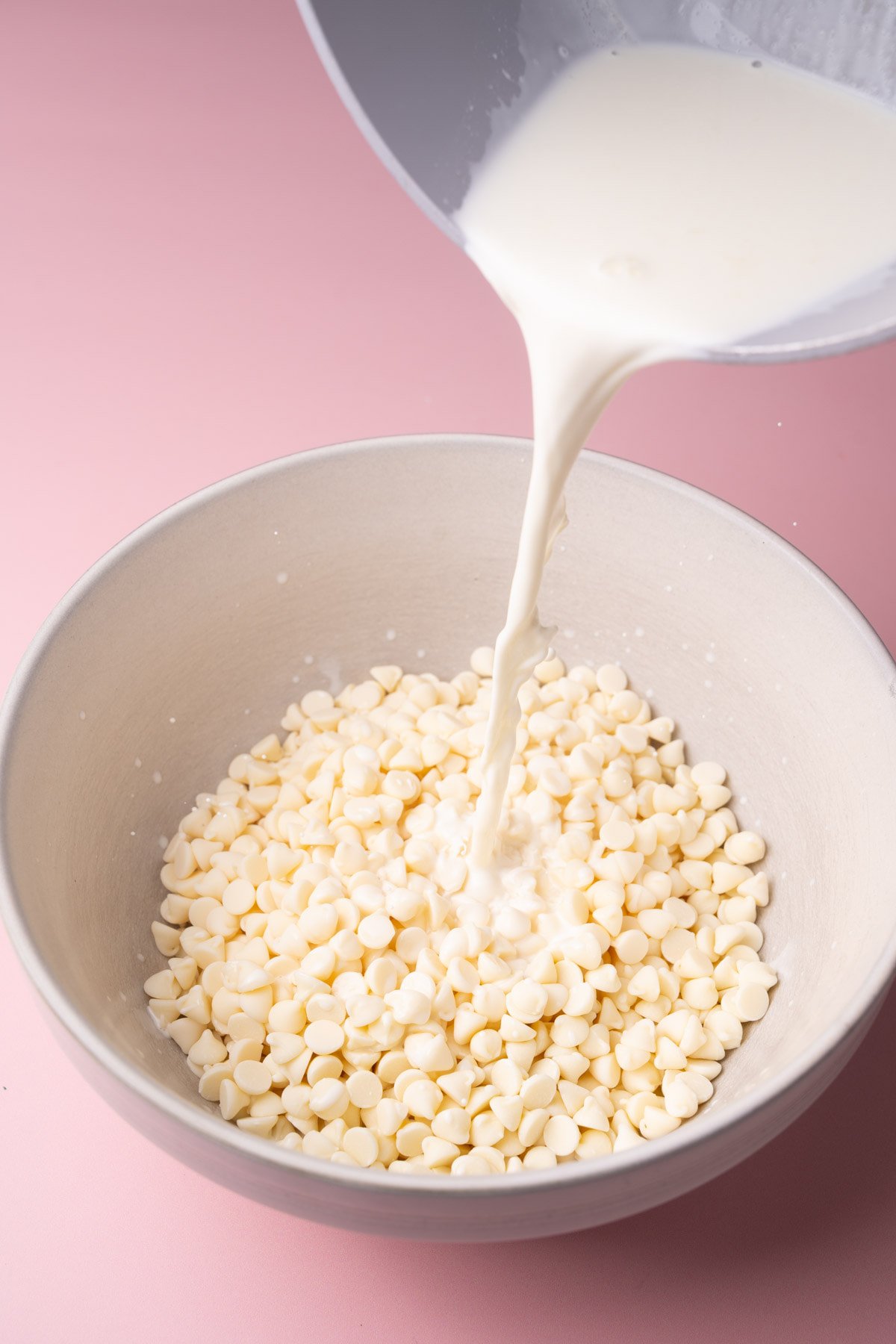 Pouring hot heavy cream over a bowl of white chocolate chips. 
