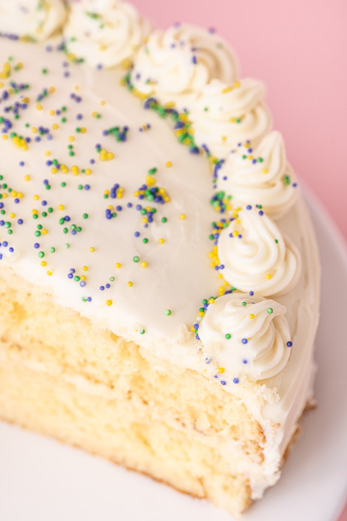 Close up of ganache made with white chocolate piped on to a white cake and topped with sprinkles.