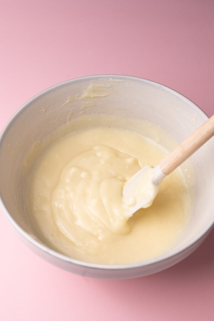 Mixing together white chocolate chips and hot heavy whipping cream to melt the chips and form a ganache. 