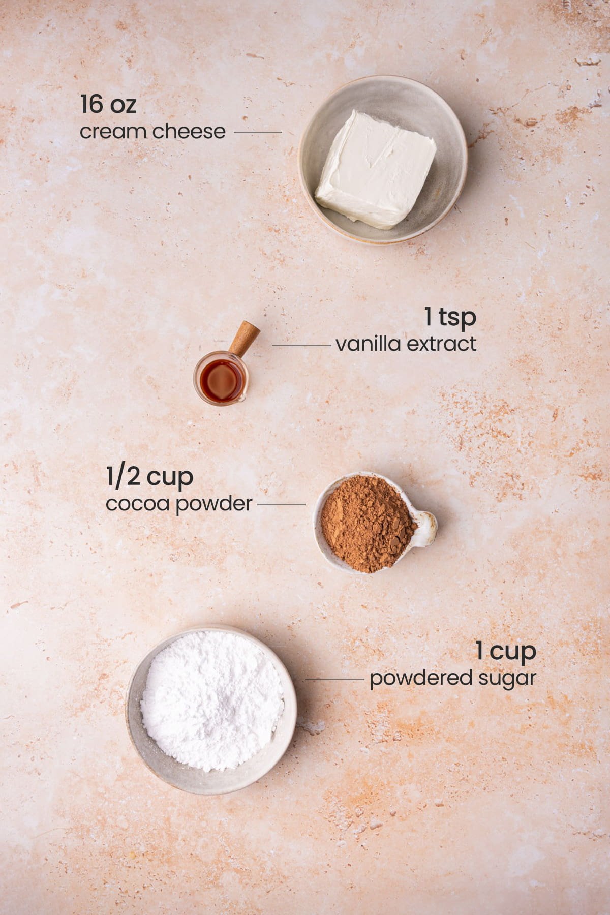Overhead view of the ingredients needed for chocolate cream cheese frosting - cream cheese, vanilla extract, cocoa powder,  and powdered sugar.