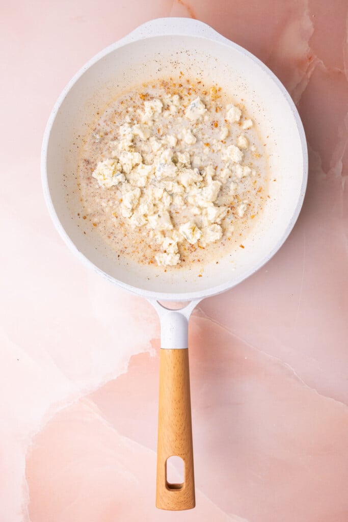 Garlic cooked in butter in a pan with milk, pepper, and crumbled gorgonzola cheese. 