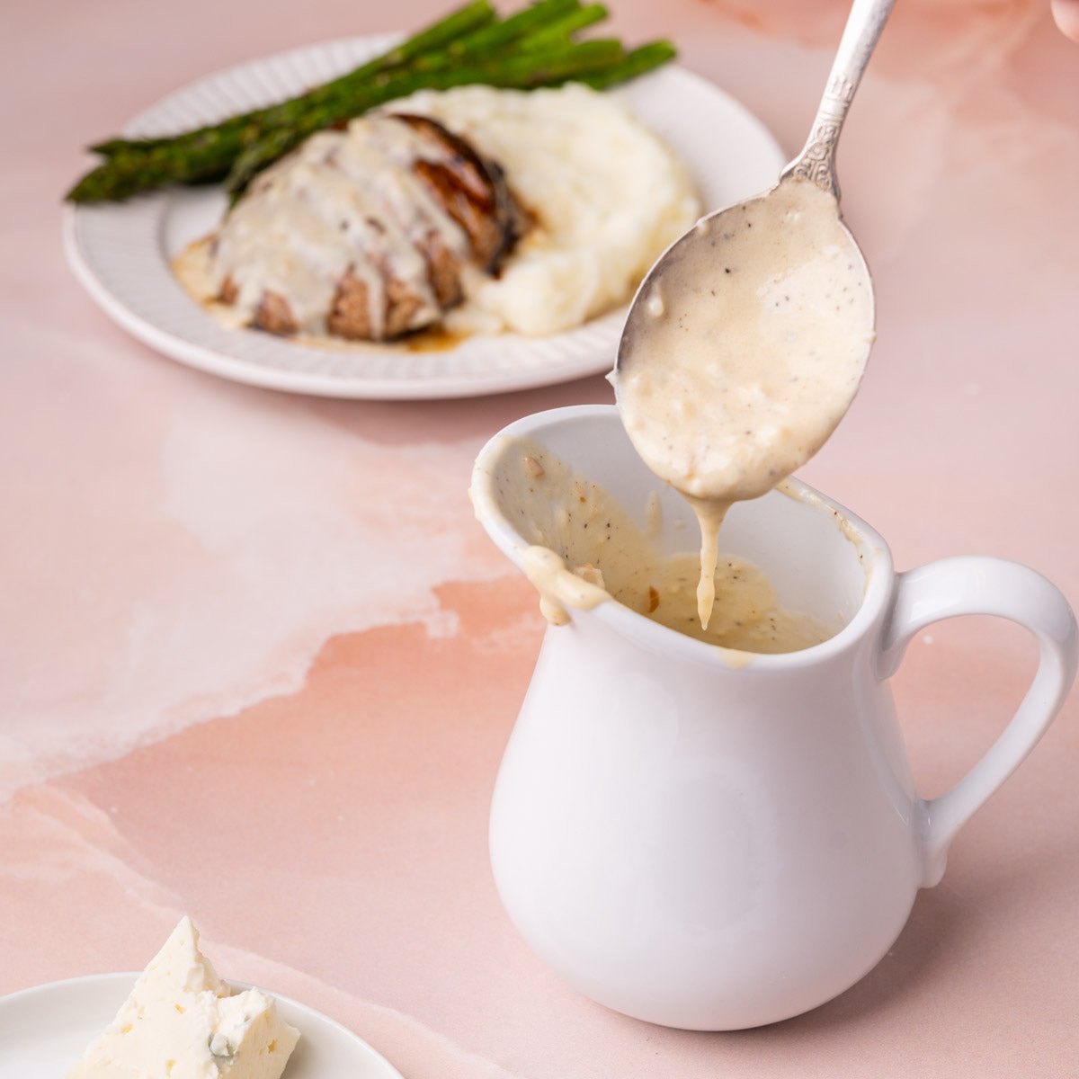 Gorgonzola cream sauce dripping off a spoon into a gravy boat to show texture.