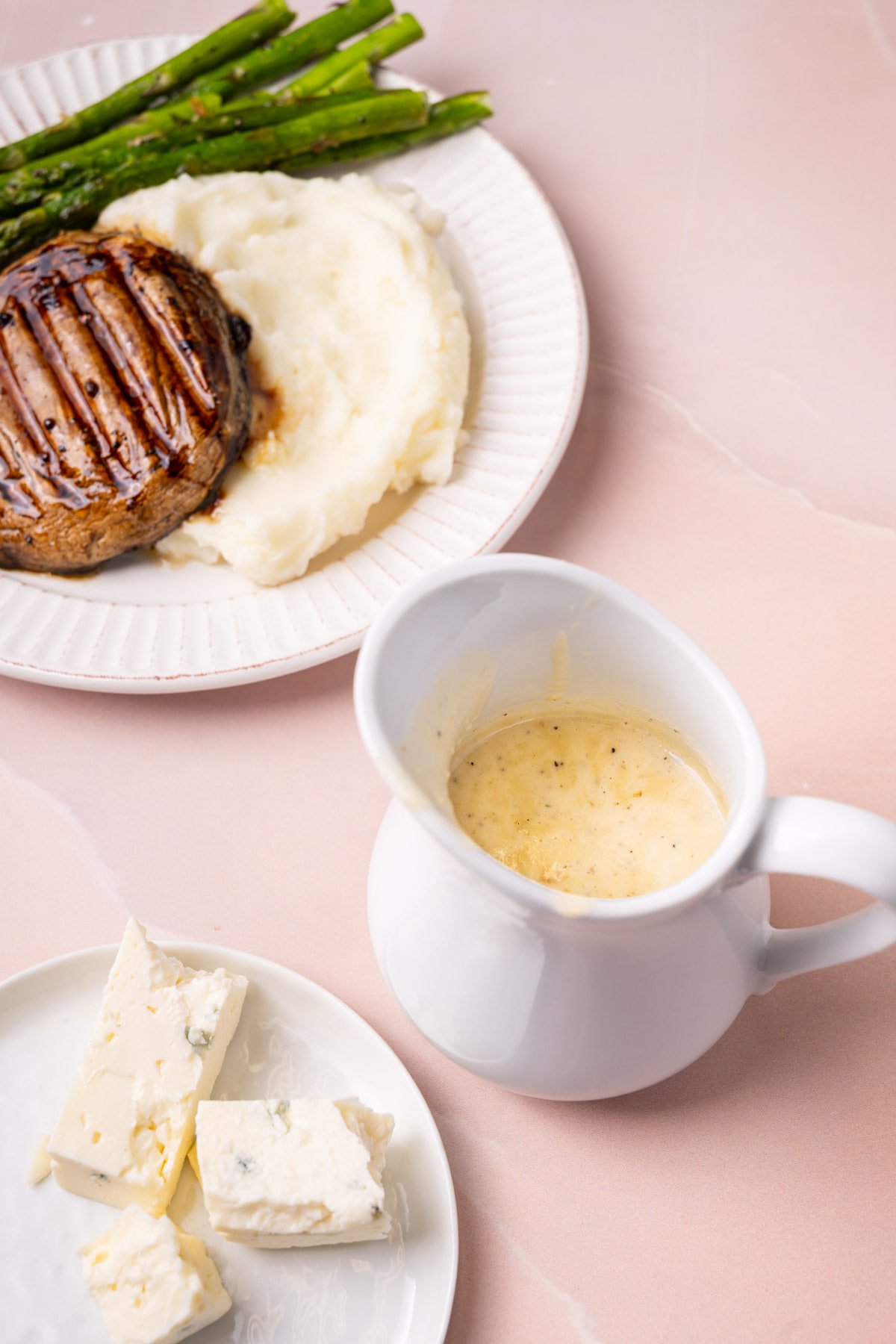 Creamy Gorgonzola cheese sauce in a gravy boat with a plated meal behind it. 