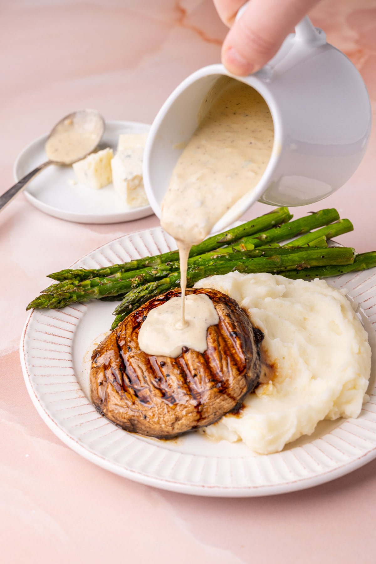 Pouring gorgonzola sauce over grilled portobello mushroom with mashed potatoes and asparagus. 
