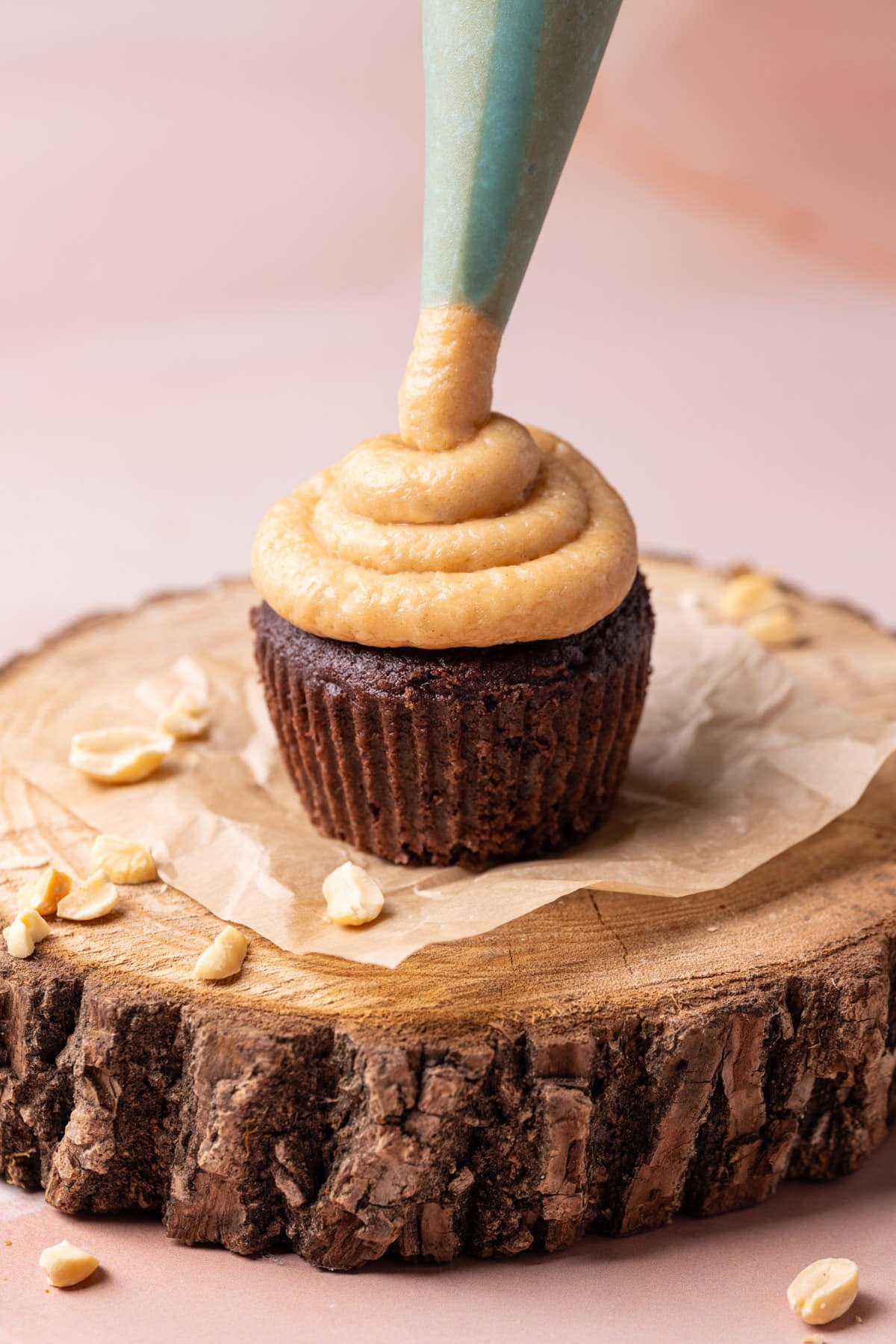 Piping peanut butter cream cheese frosting onto a chocolate cupcake. 
