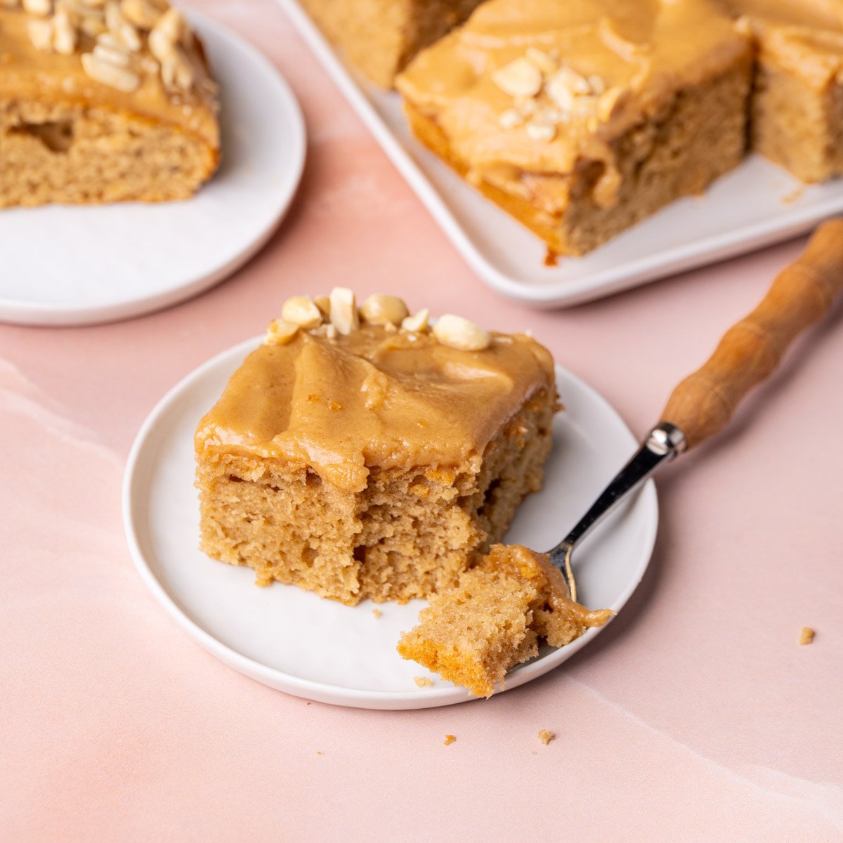 Square slice of peanut butter cake on a plate with forkful on the side.