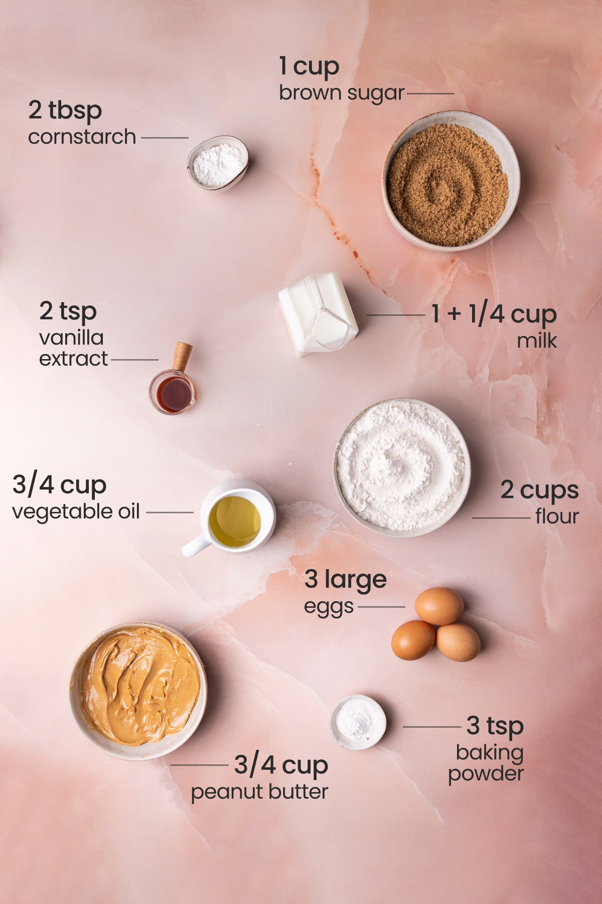 Overhead view of the ingredients needed for a peanut butter sheet cake - cornstarch, brown sugar, vanilla extract, milk, vegetable oil, eggs, flour, baking powder, and peanut butter.