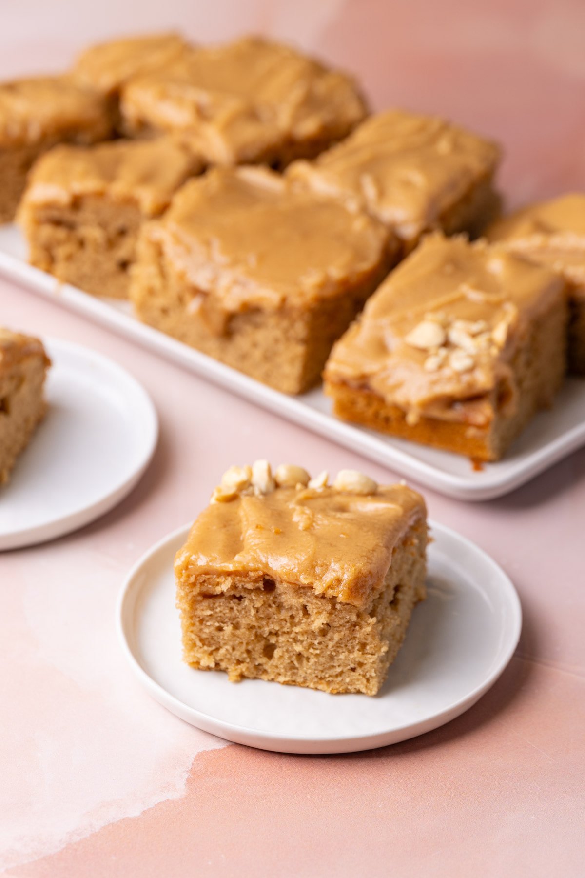 Slice of sheet pan peanut butter cake with the rest of the cake in the background. 