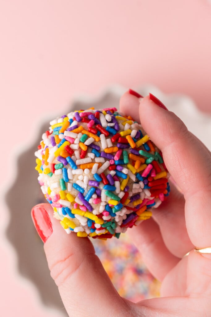 Close up of sugar cookie dough ball completely coated in rainbow sprinkles.