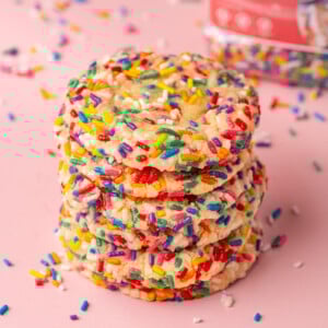 Stack of sprinkle sugar cookies with jar of rainbow sprinkles in the background.
