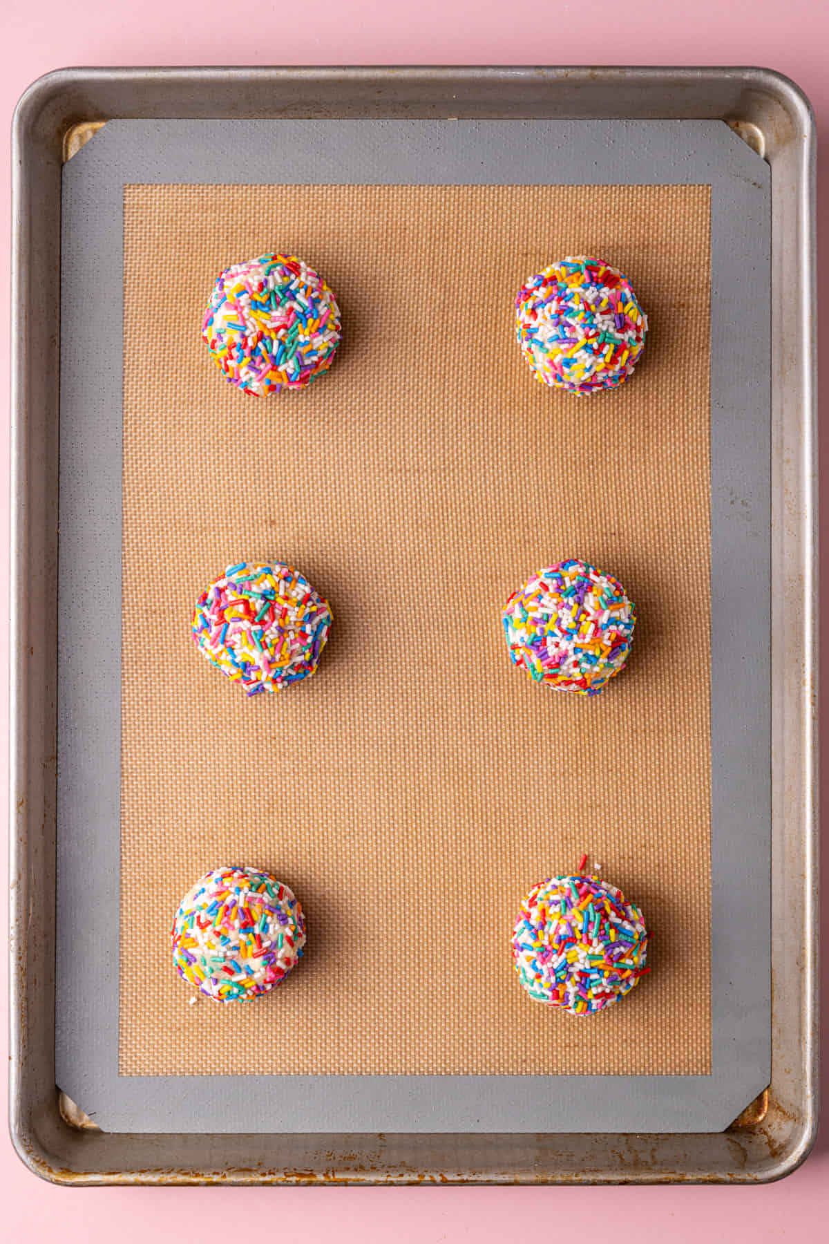 Sugar cookies coated in sprinkles lined up on a baking sheet ready to bake in the oven.