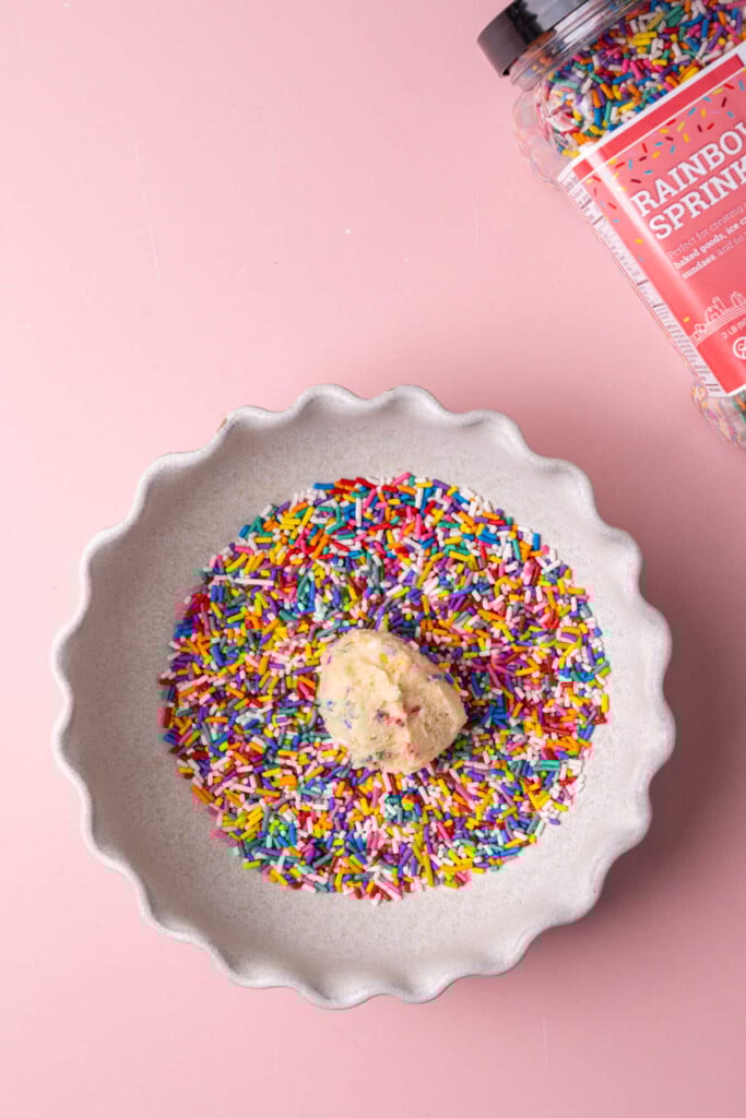 Rolling sugar cookie dough ball in sprinkles to coat it completely.