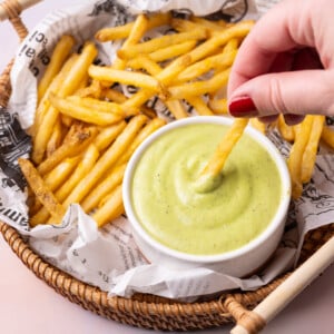 Close up action shot of dipping a crispy French fry into homemade avocado-based ranch dressing.
