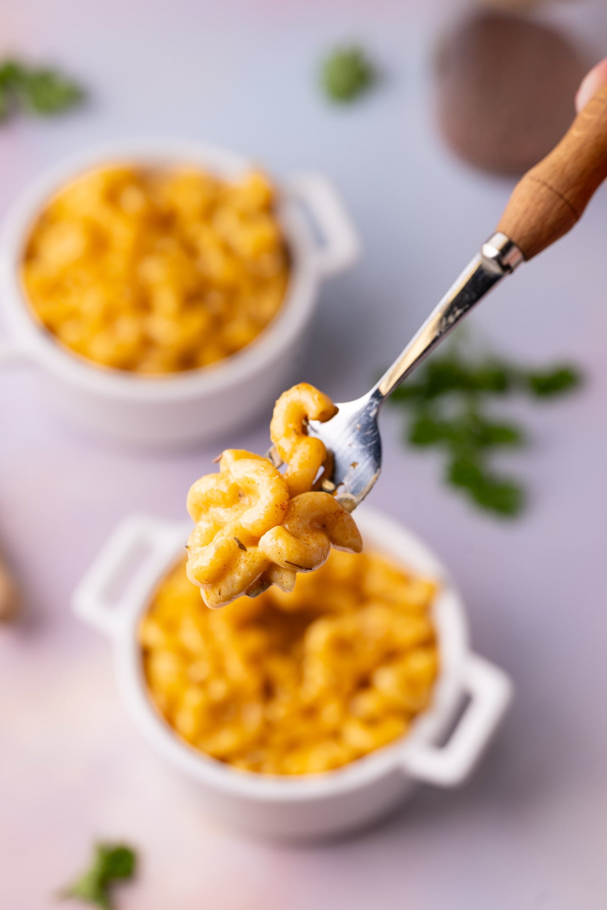 Spicy mac n cheese on a fork with two bowl and Cajun seasoning jar in the background.