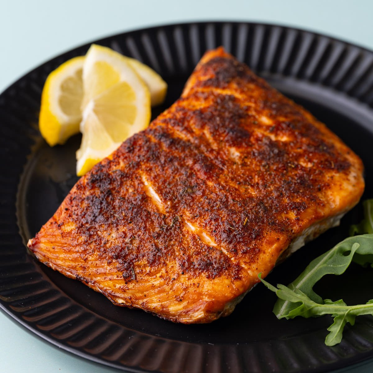 Close up of roasted Cajun salmon on a plate with lemon wedges.