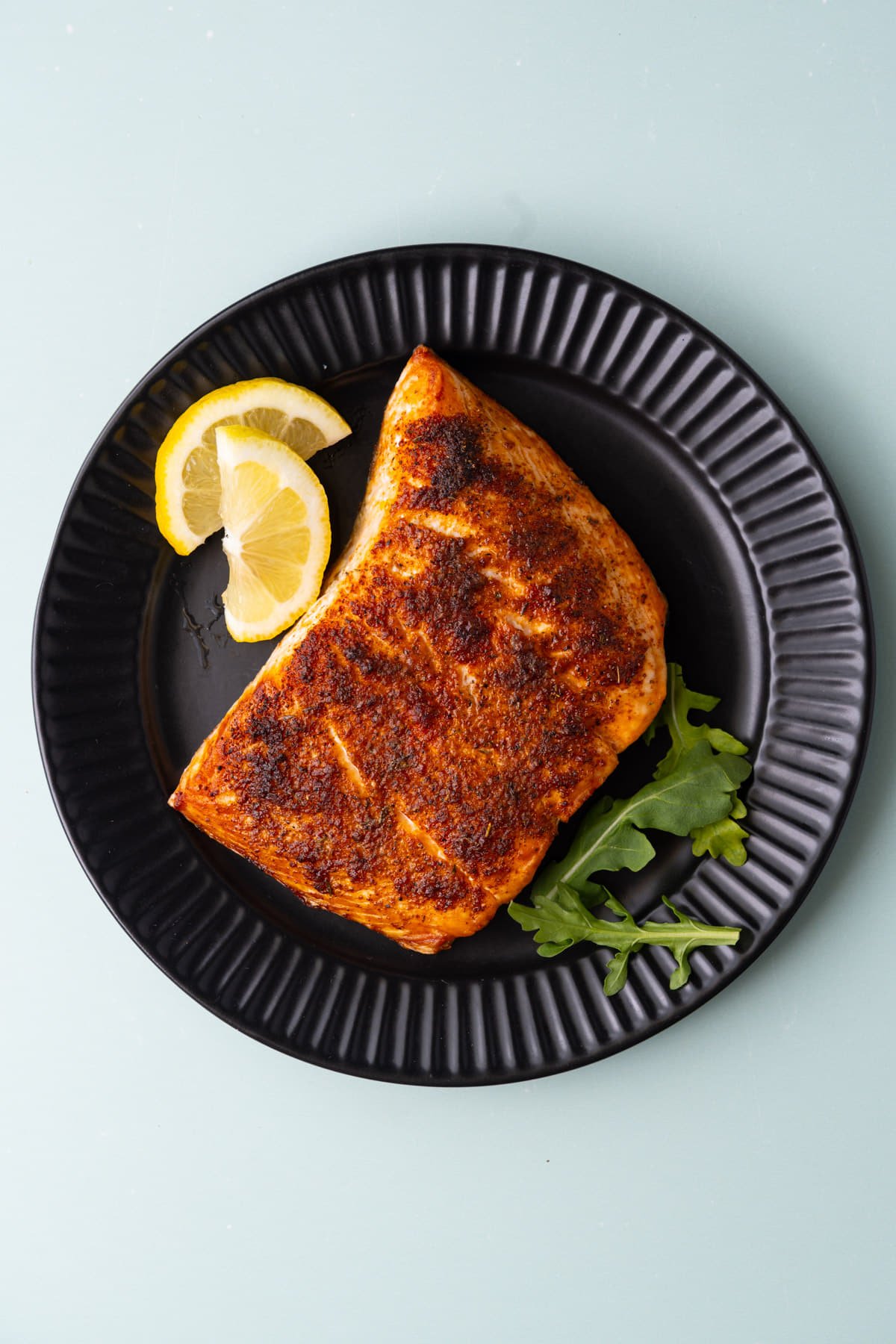 Overhead image of Cajun roasted salmon on a plate with lemon wedges and greens. 