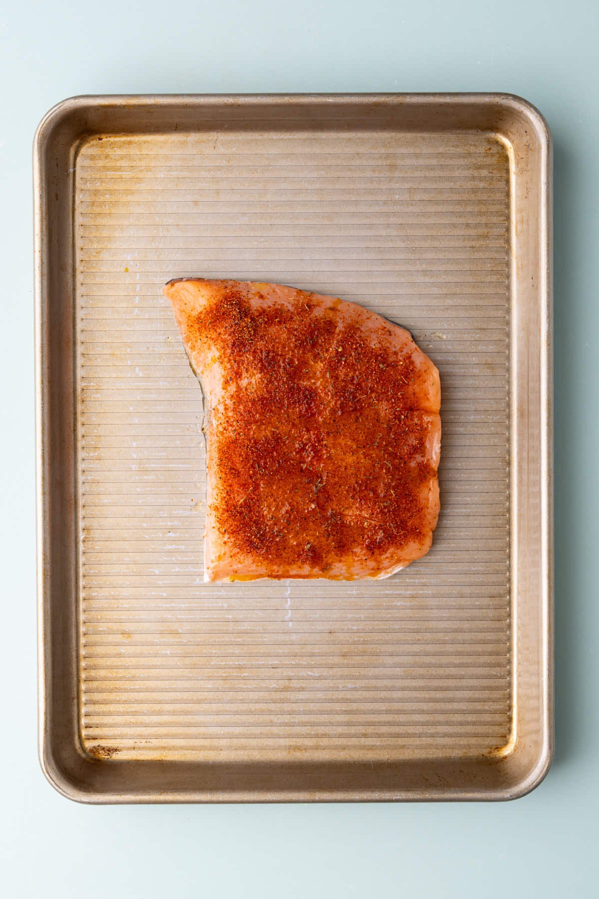 Samon on a baking sheet seasoned with lemon juice, olive oil, and Cajun seasoning. 