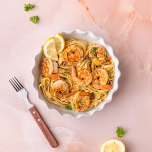 Cajun shrimp scampi plated with pasta and two lemon wedges with a fork off to the side.