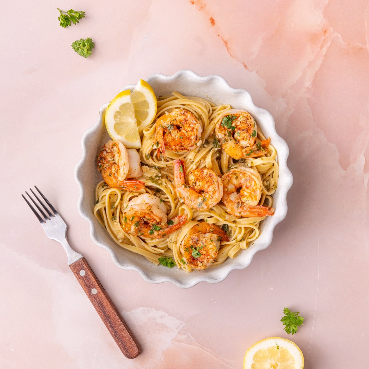 Cajun shrimp scampi plated with pasta and two lemon wedges with a fork off to the side.