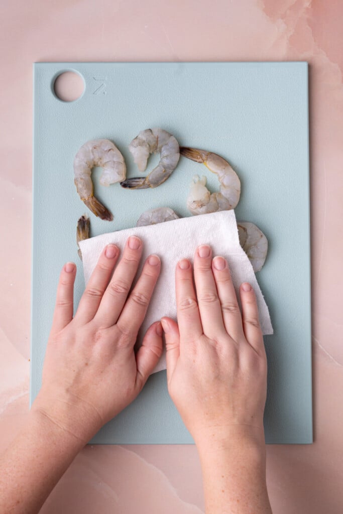 Using a paper towel to blot dry raw shrimp to reduce moisture. 