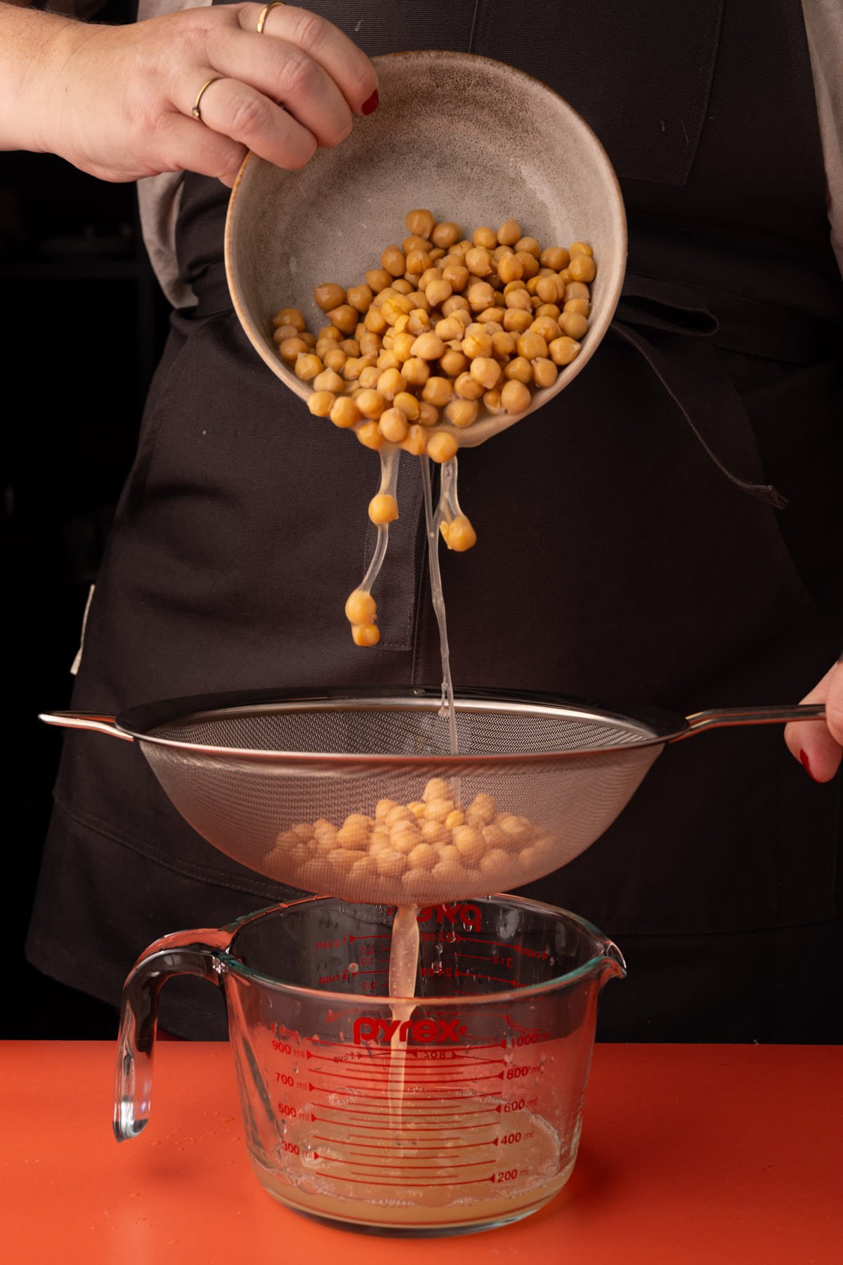 Straining can of chickpeas through a sieve and catching the liquid in a measuring cup underneath.