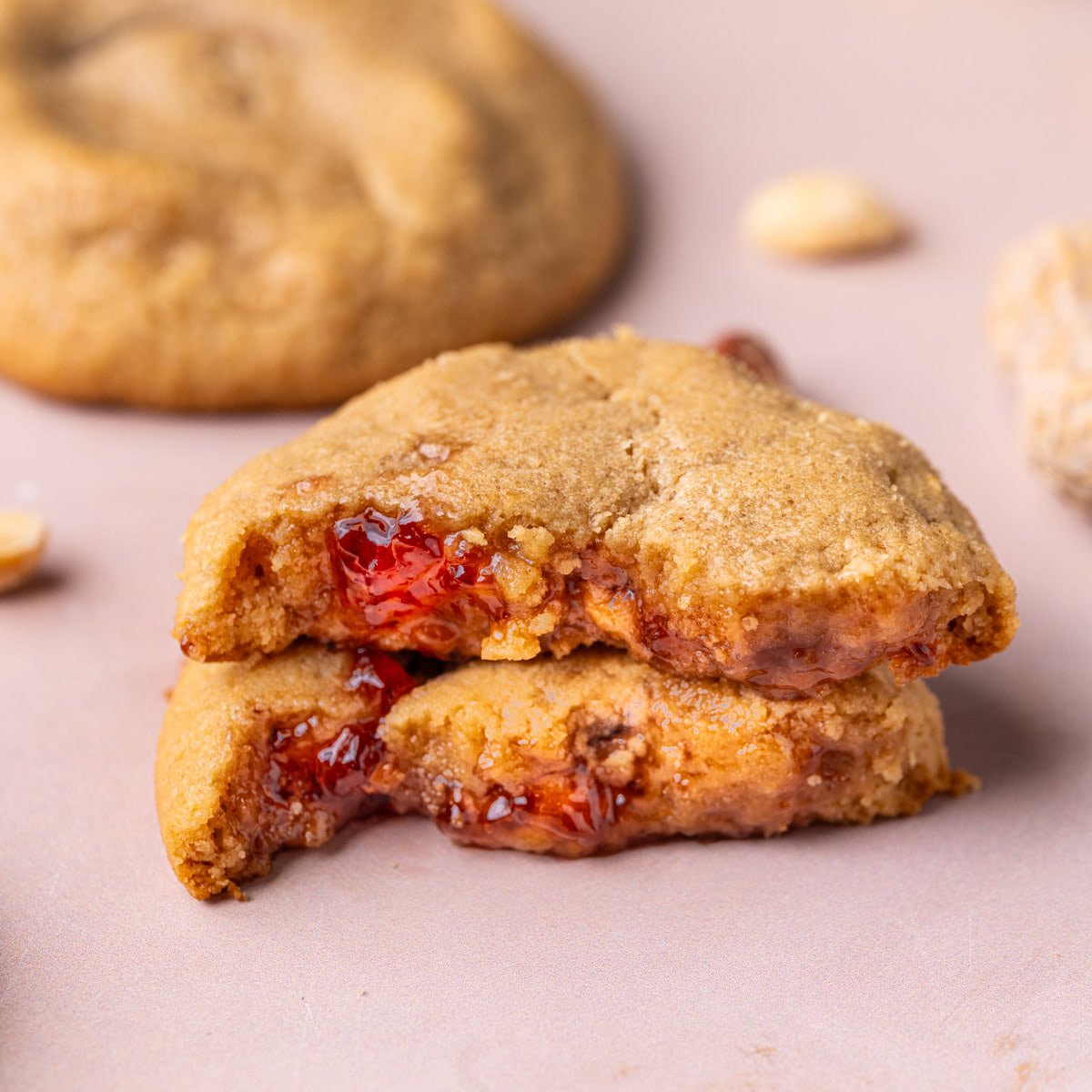 Peanut butter and jelly cookie broken in half, with two halves stacked atop each other to reveal the jelly on the inside.