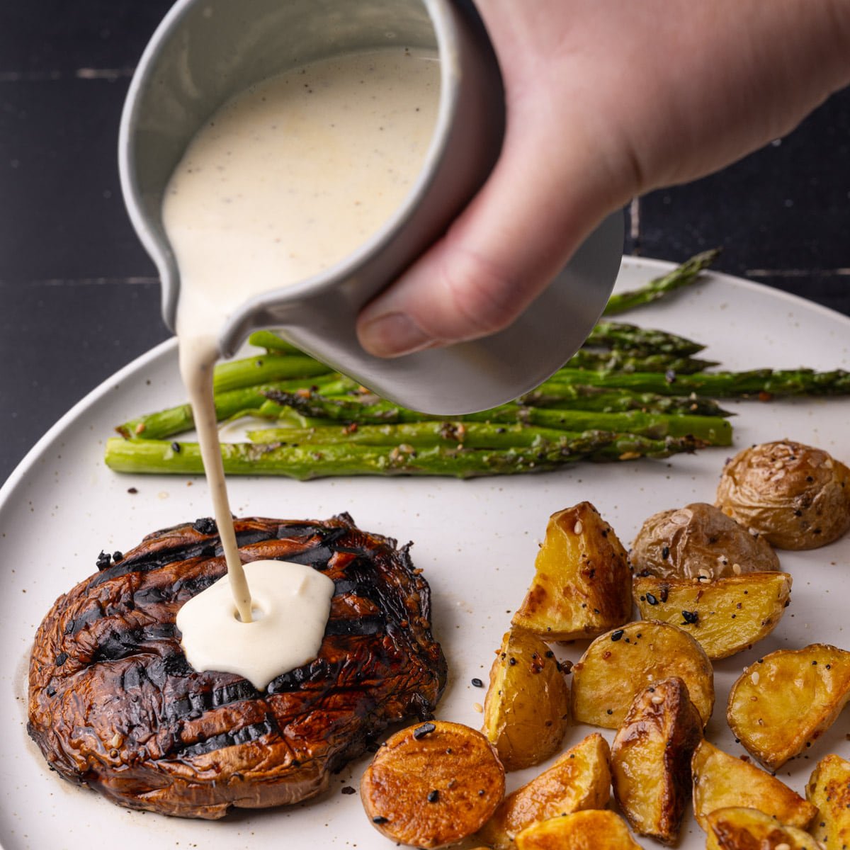 Pouring sherry cream sauce over portobello mushroom on dinner plate.