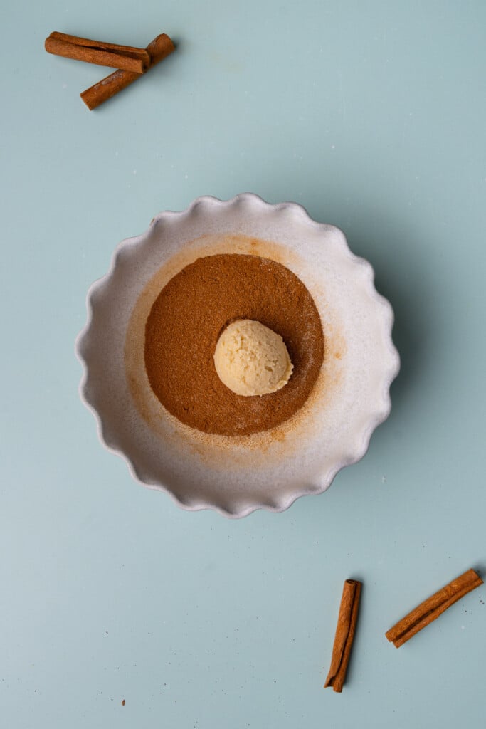 Cookie dough placed in a shallow bowl on cinnamon and sugar. 