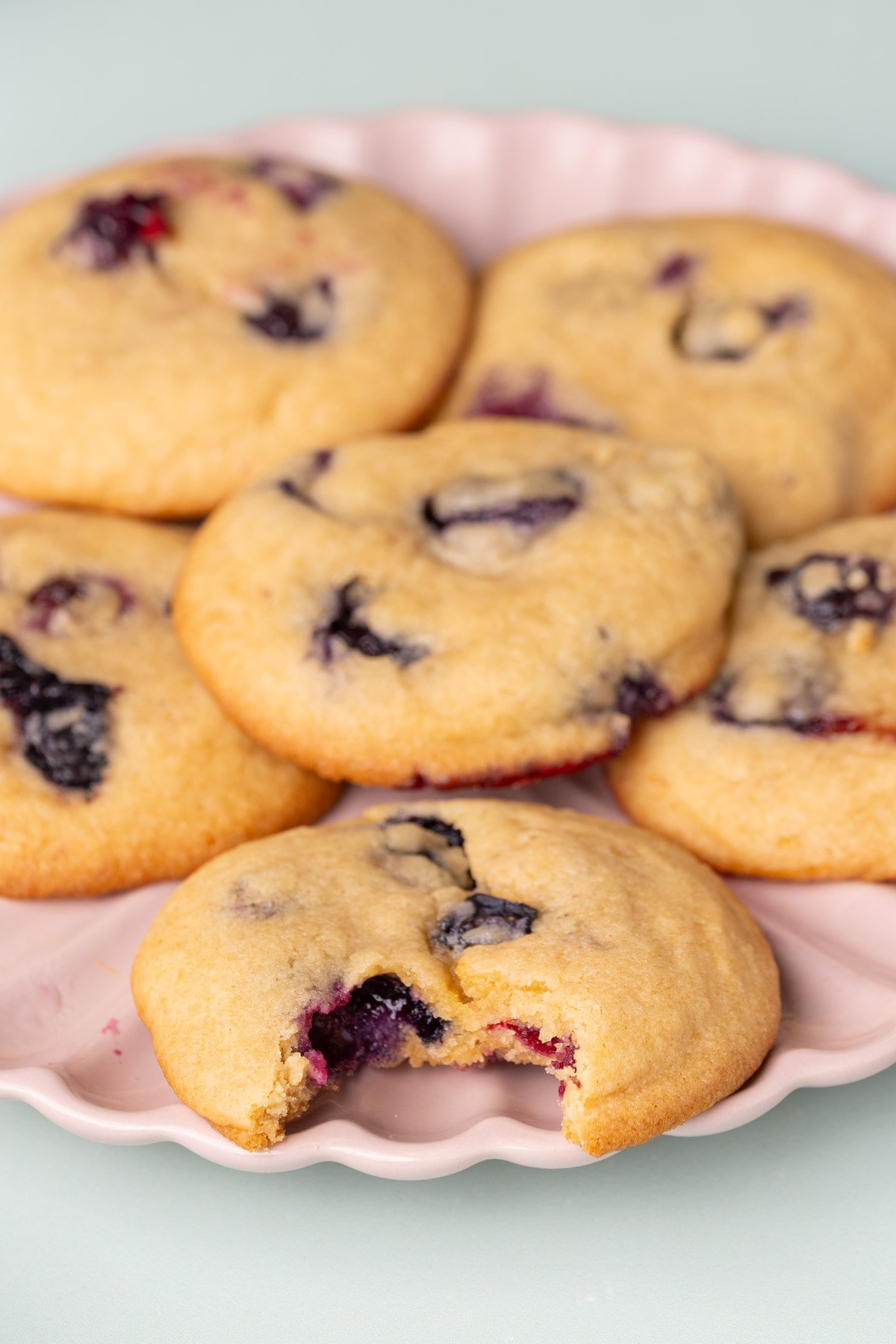 A plate of cookies with the front one having a bite taken out of it to reveal the fresh blueberries inside. 