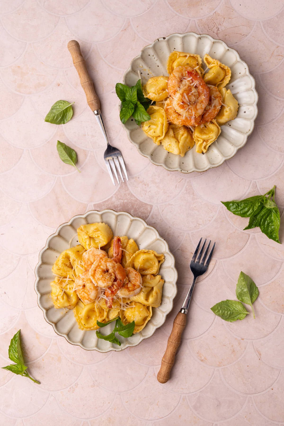 Overhead images of two plated of shrimp tortellini surrounded by basil leaves. 