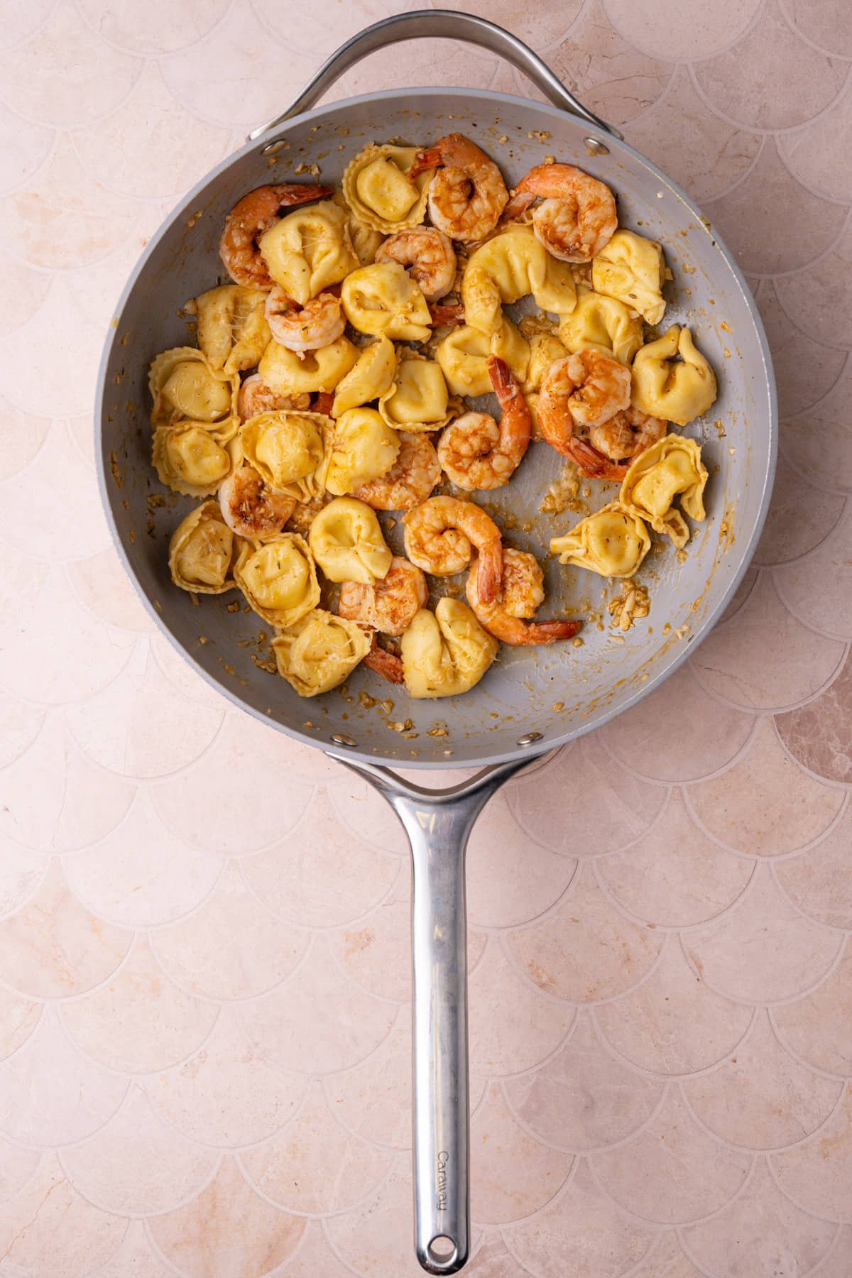 Tossing cooked tortellini with pan-fried shrimp, butter, lemon juice, and garlic. 