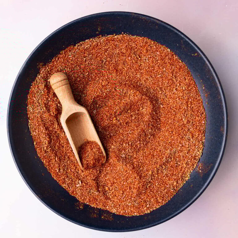 Shallow bowl of spice blend with a wooden seasoning spoon in it.