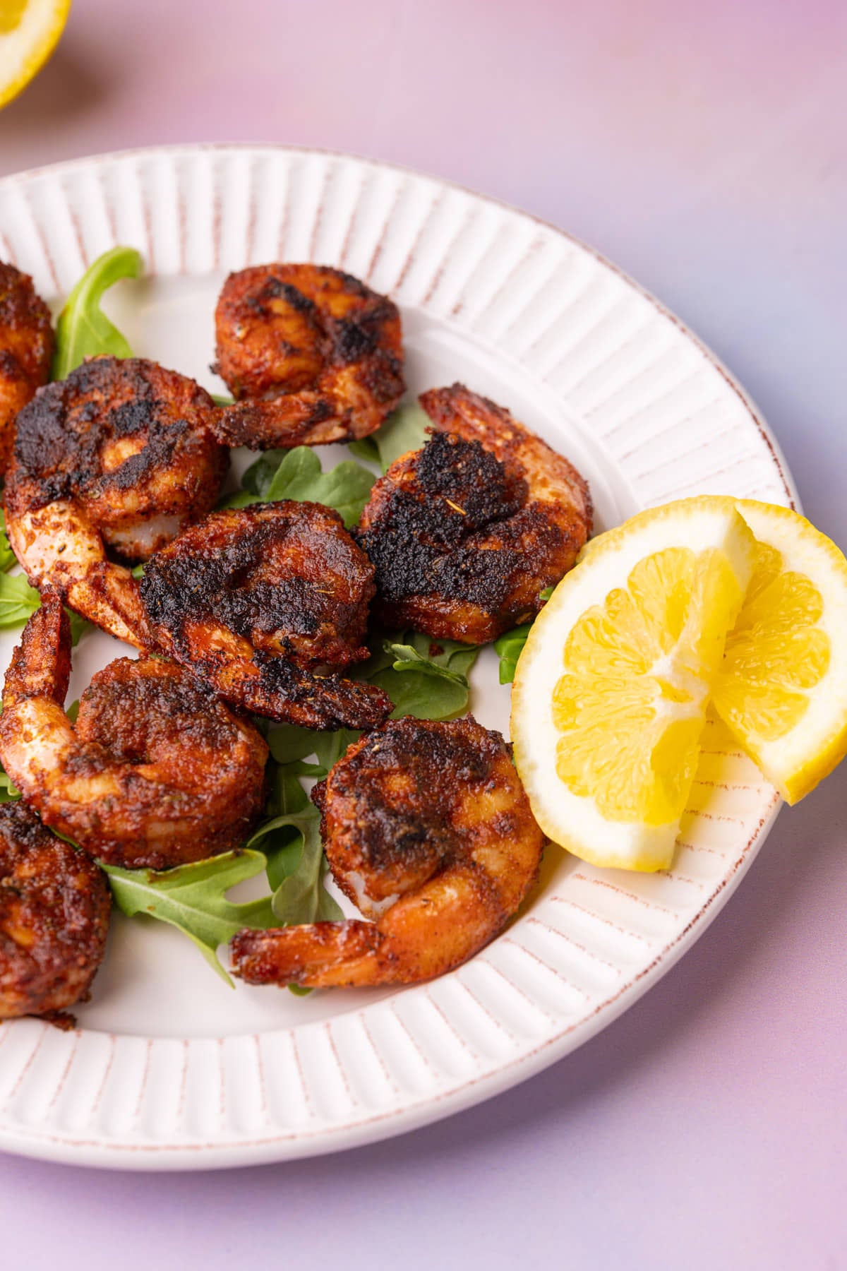 Close up of blackened shrimp on a plate next to two lemon wedges and on a bed of arugula.
