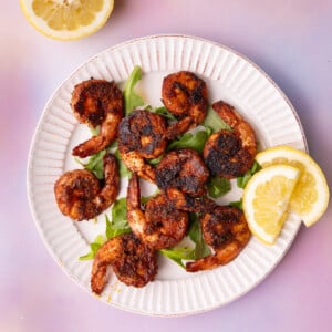 White plate with scalloped edges with blackened shrimp and lemon wedges.