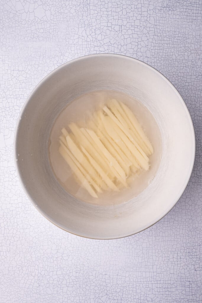Soaking hand-cut fries in water to remove excess starch.