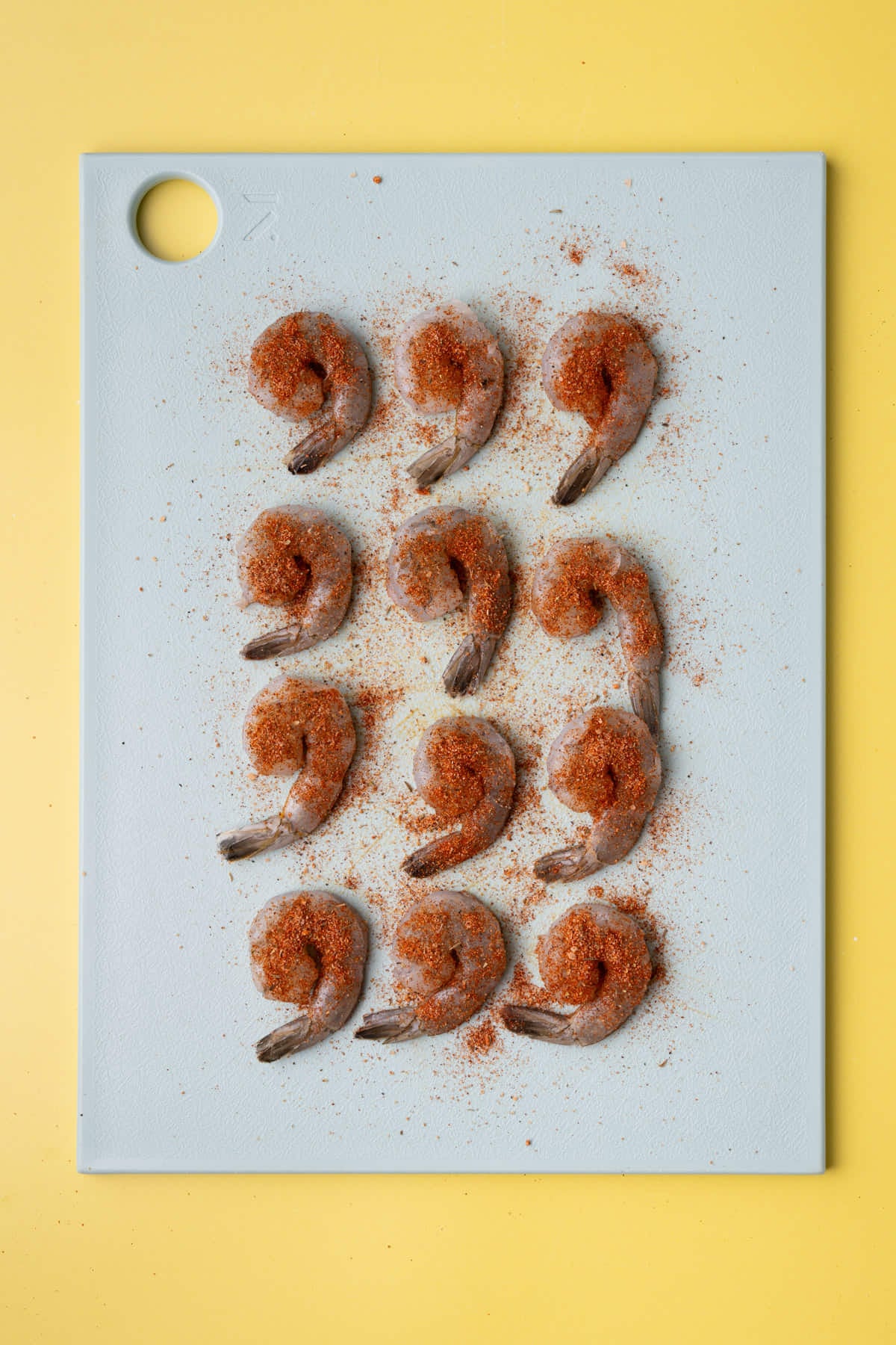Raw shrimp lined up on a chopping board with Cajun season covering both sides.
