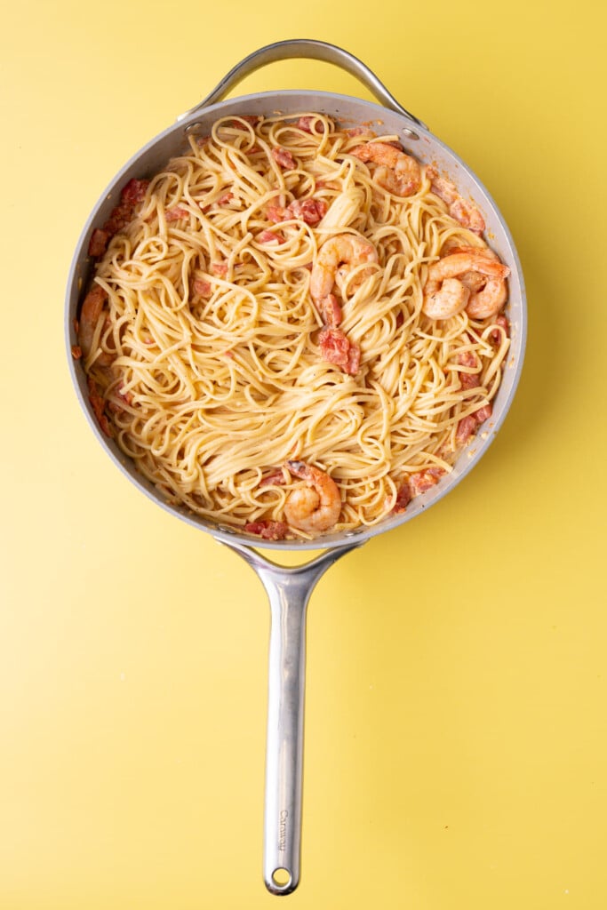 Tossing pasta in a creamy Cajun sauce made in a pan with shrimp.