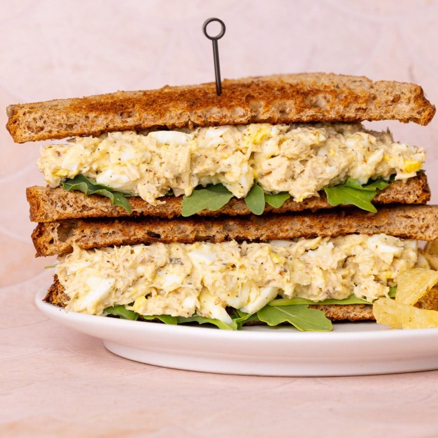 Tuna and Egg Sandwich cut in half and stacked on a plate with potato chips.