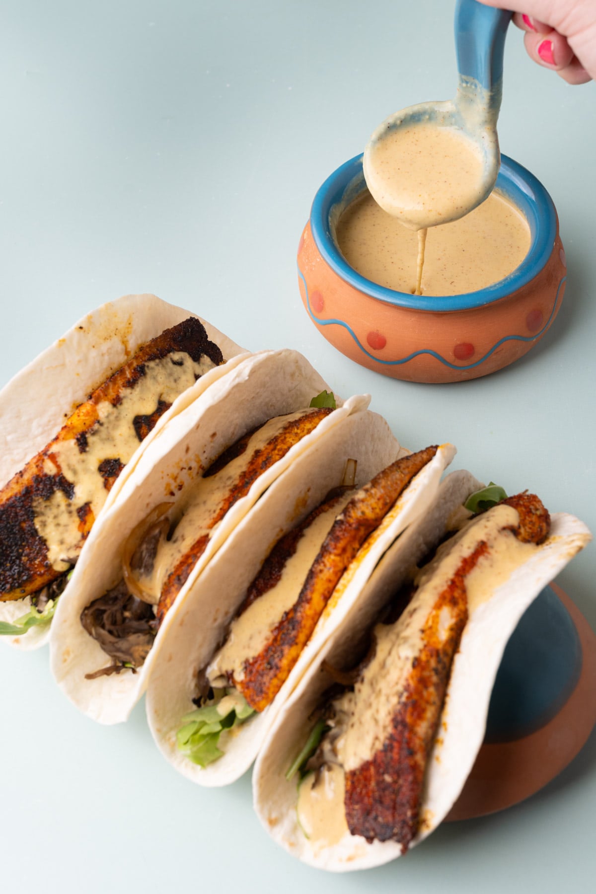 Fish tacos with creamy sauce dripping off a spoon in the background.