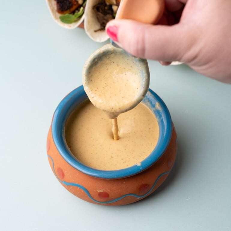 Pineapple fish taco sauce in a small pot dripping off a spoon to show the consistency.