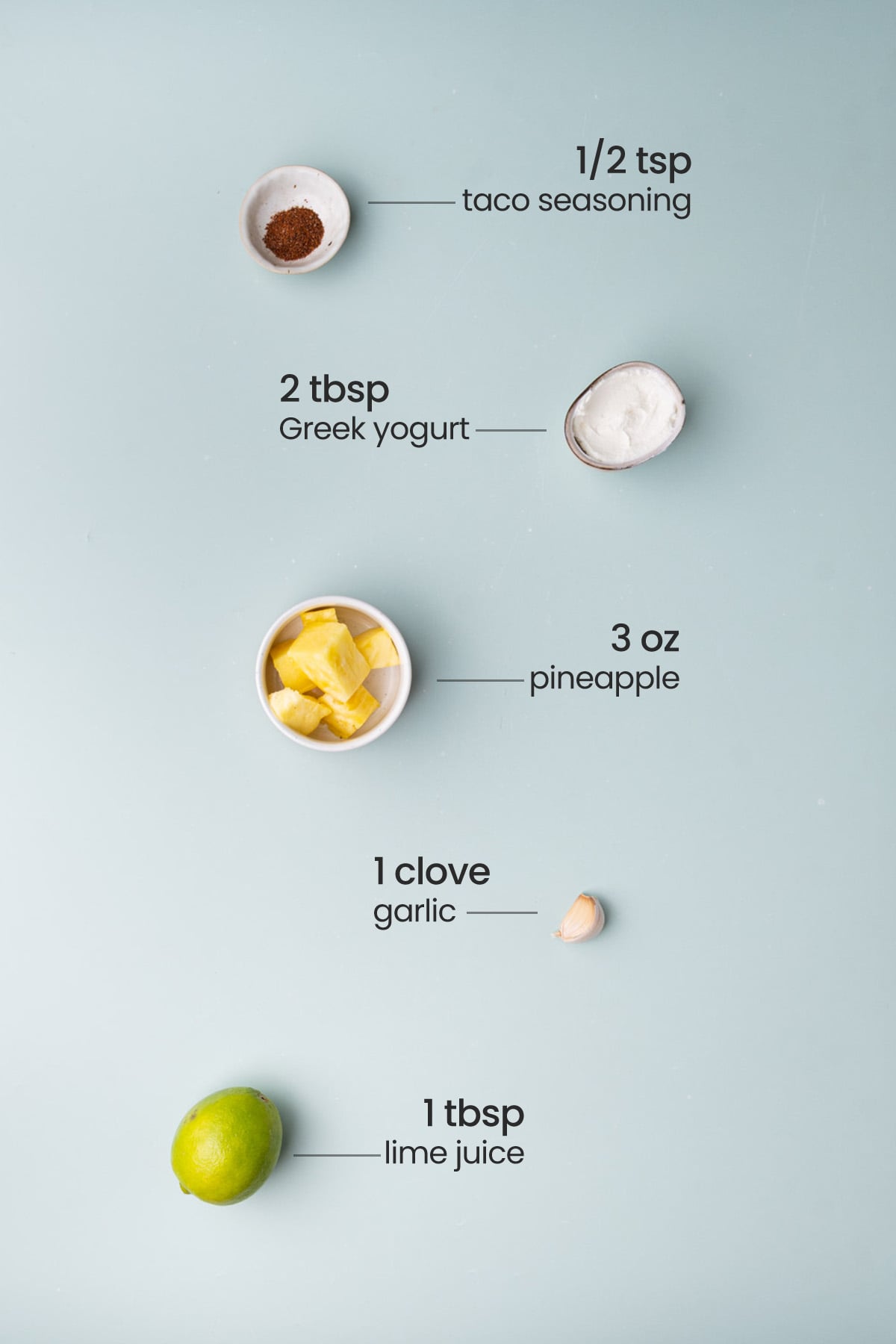 Overhead view of the ingredients needed for fish taco sauce - taco seasoning, Greek yogurt, pineapple, garlic, and lime juice.
