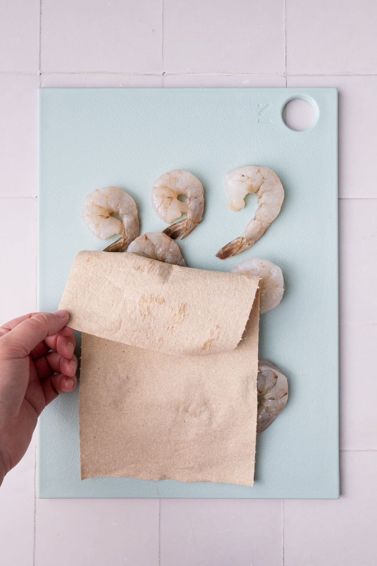 Prepping shrimp to fry in garlic and oil by peeling it and blotting it with a paper towel.