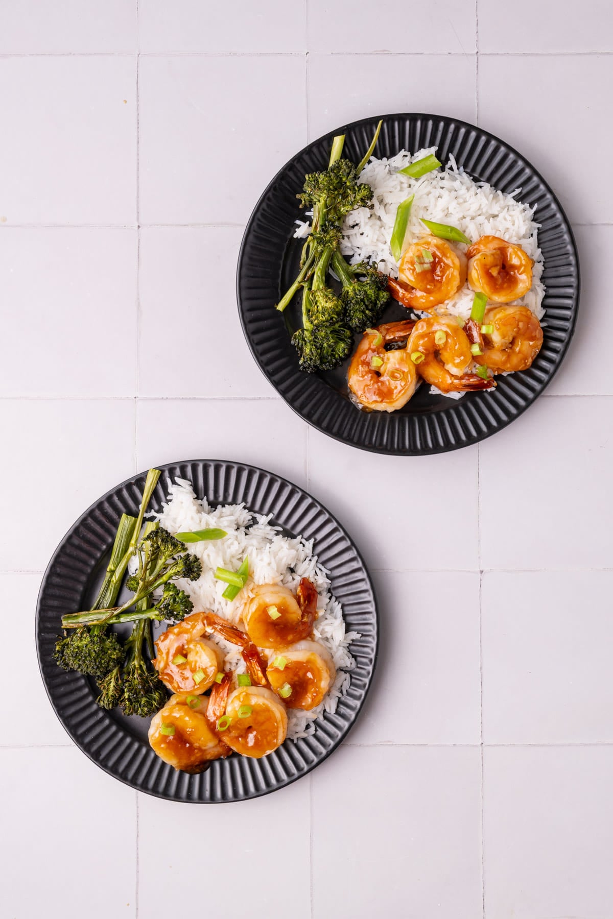 Two black plated with generous portions of white rice, broccolini, and garlic honey shrimp.