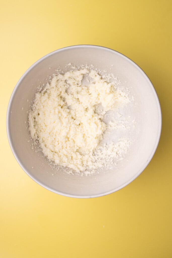 Butter and sugar creamed together until light and airy in a large mixing bowl on yellow background. 