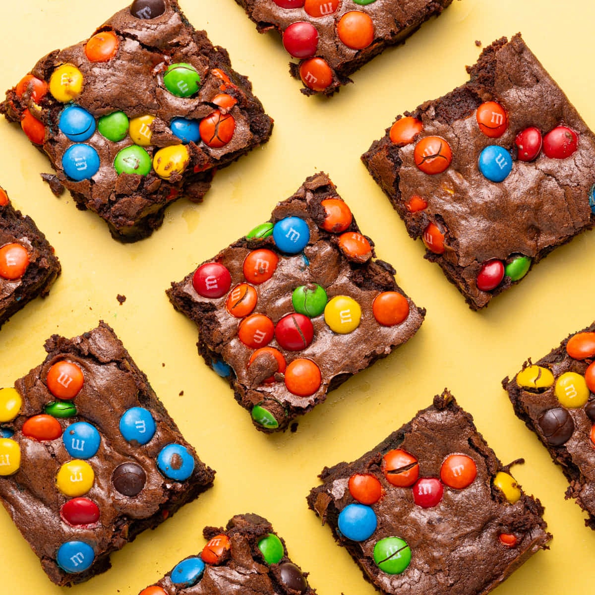 Colorful brownies with M&M's lined up on a yellow background.