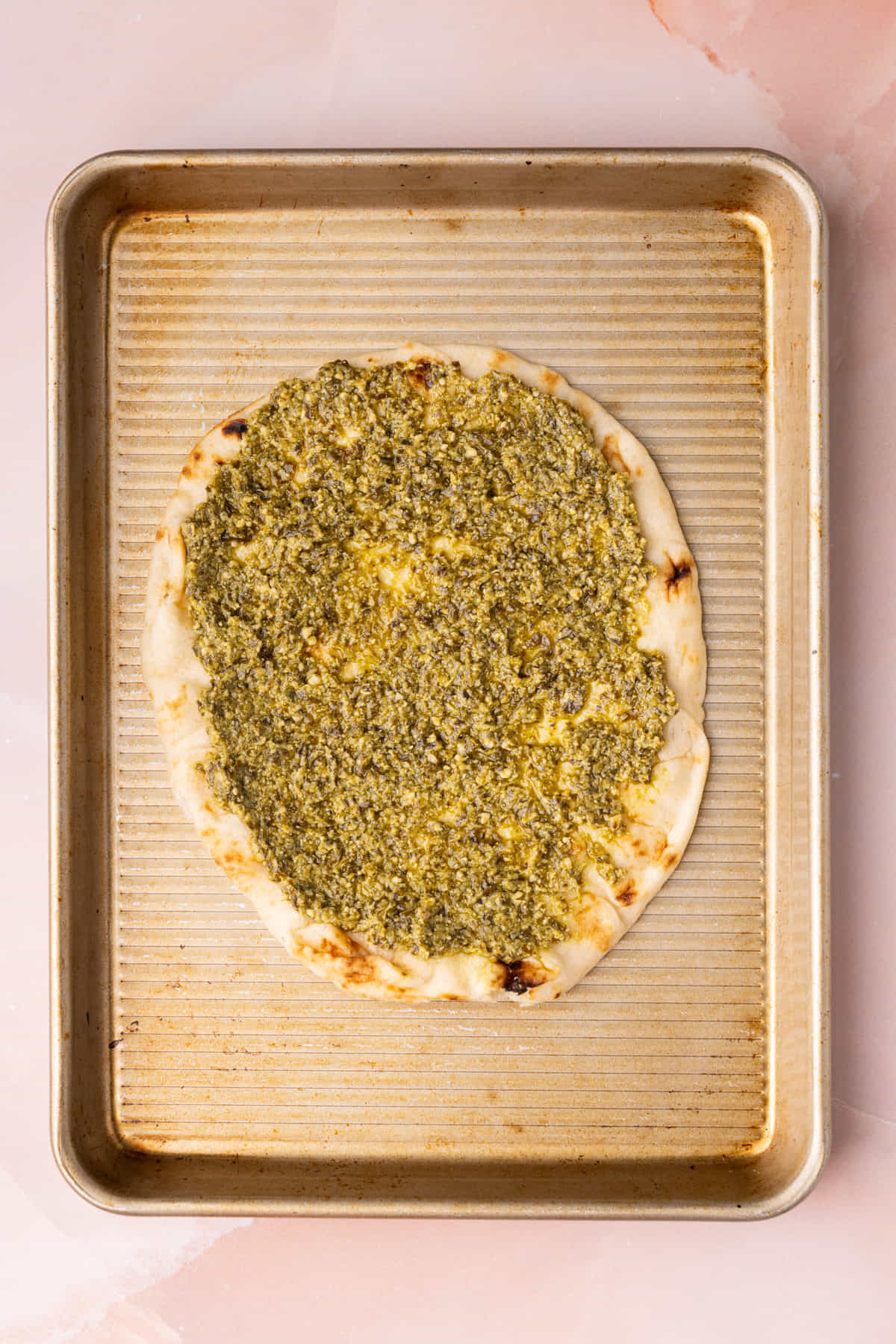 Pesto spread across a piece of naan bread in an even layer on a baking sheet.