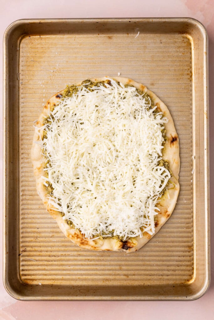 A piece of naan bread with thin layer of pesto and mozzarella and Parmesan cheeses.